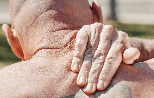 Shirtless person reaching over their shoulder to rub their trapezius.